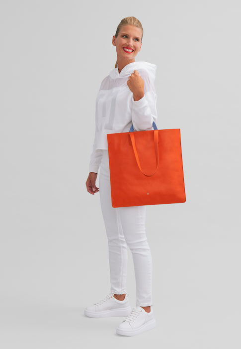 Woman smiling holding large orange tote bag in white outfit on neutral background