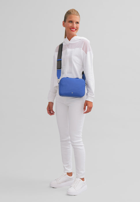 Woman in white outfit with blue crossbody bag and sneakers against gray background