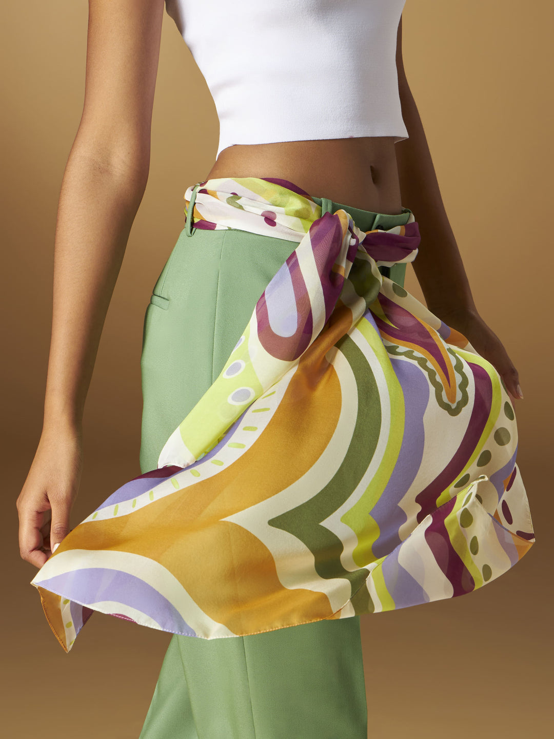 Fashionable woman wearing colorful silky scarf tied around her waist with green pants and white crop top