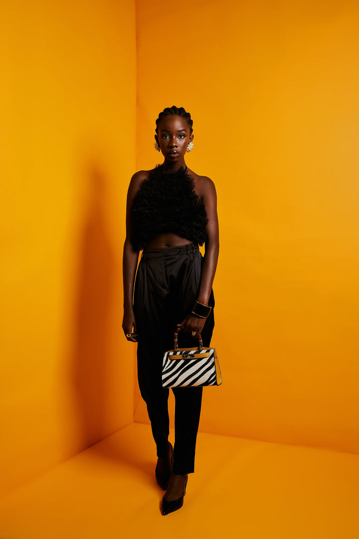 Fashionable woman in black elegant outfit holding zebra print handbag against bright orange background