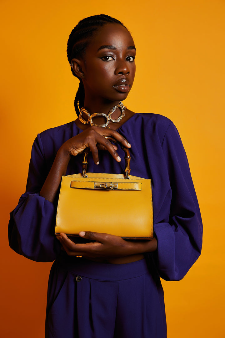 Person holding a yellow handbag with bamboo handle against an orange background