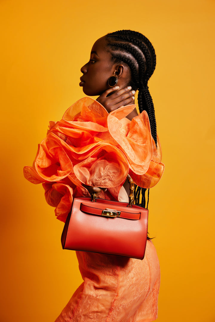 Woman in vibrant orange outfit holding a stylish red handbag against a yellow background