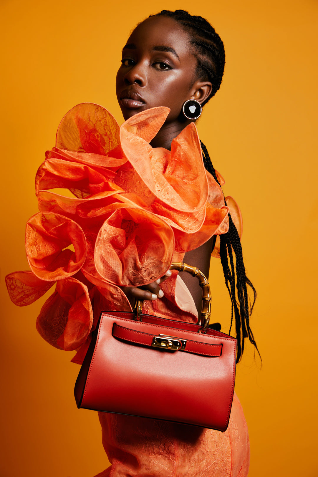 A fashionable woman in an orange dress holding a red handbag against an orange background