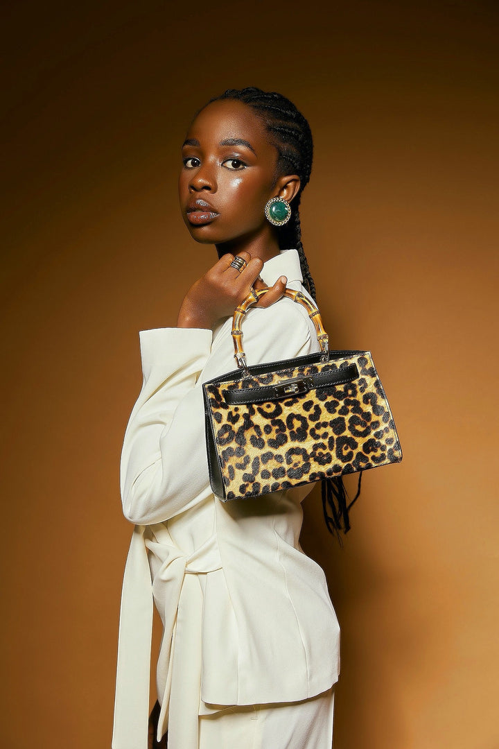 Woman in white suit holding a leopard print handbag against a brown background