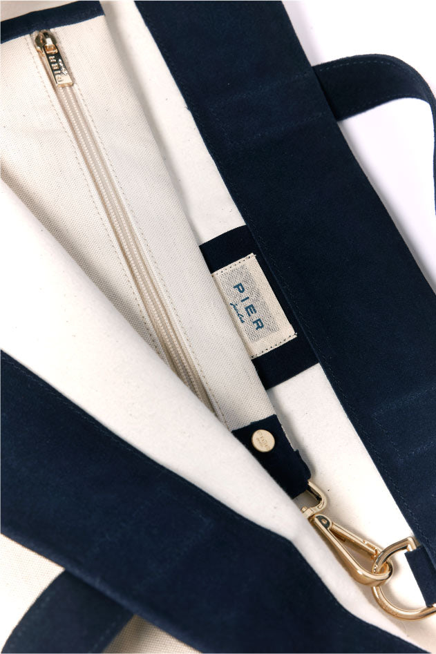 Close-up of a stylish navy blue and white canvas tote bag with a gold zipper and clasp