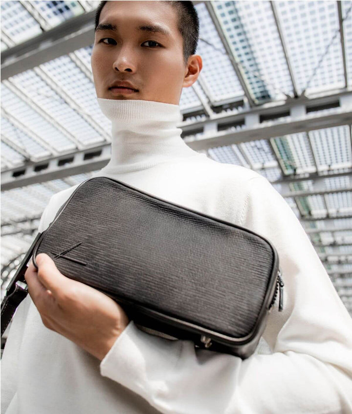 Young man holding a black leather shoulder bag under a modern glass roof