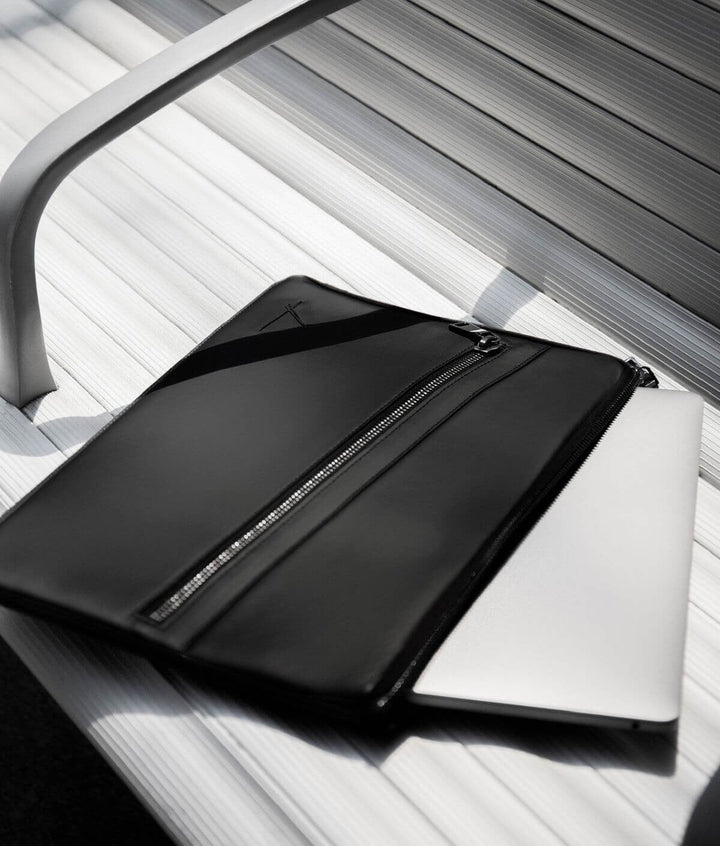 Black leather laptop sleeve with zipper pocket on a white bench