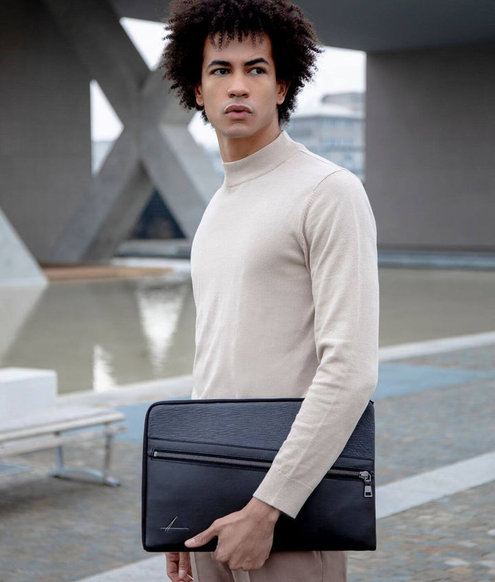 Young man holding black portfolio in modern urban setting