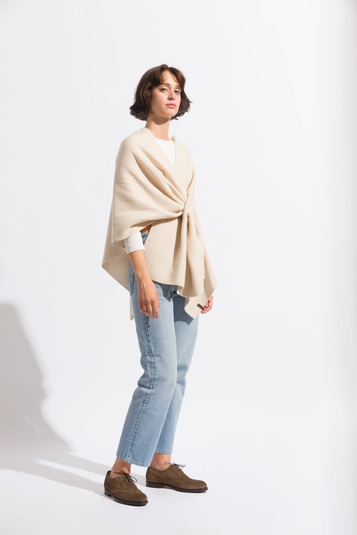 Woman wearing beige shawl over white top and jeans against white background