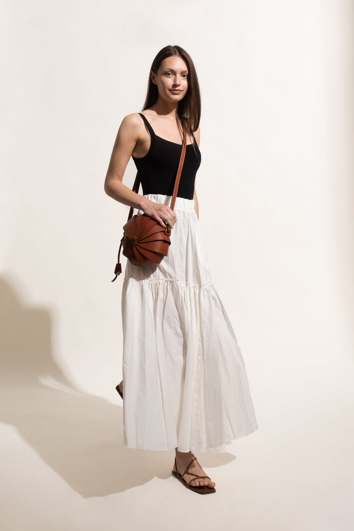 Woman in black top and white skirt with brown shoulder bag on light background