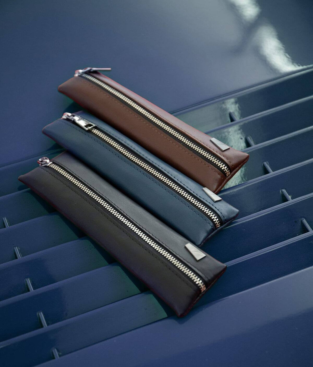 Leather zipper pouches in brown, blue, and black on a blue surface