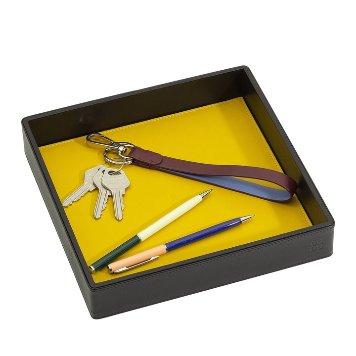 Black tray containing keys with a leather keychain and assorted pens on a yellow surface