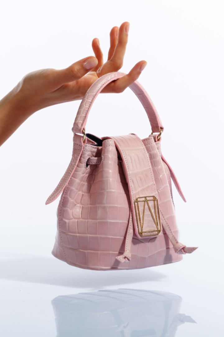 Hand showcasing a small pink leather handbag with gold buckle against white background