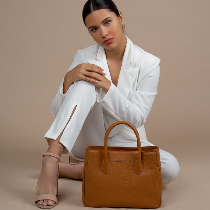 Woman in white suit poses with tan handbag against beige background