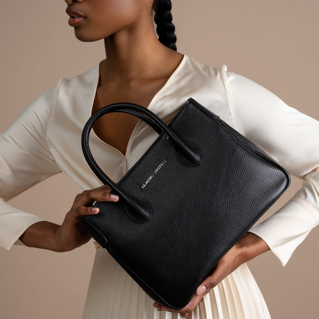 Woman holding a black leather handbag against a beige background