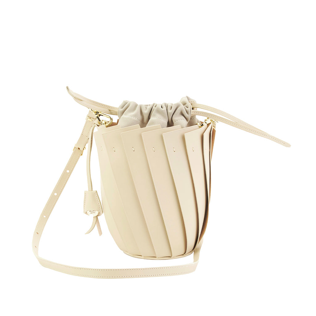 Beige drawstring bucket bag with pleated leather design and adjustable strap