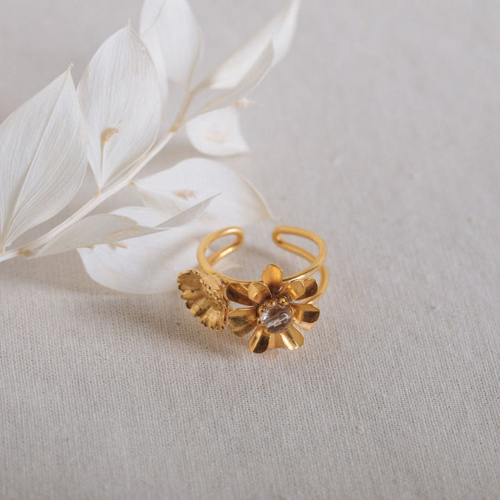 Gold floral ring on beige background with white dried leaves