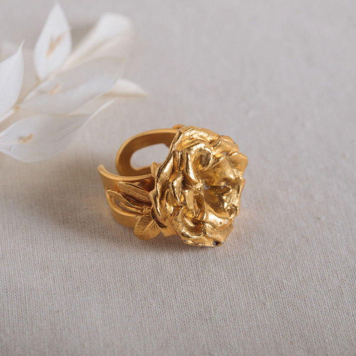 Gold flower-shaped ring on beige fabric background with white decorative leaves