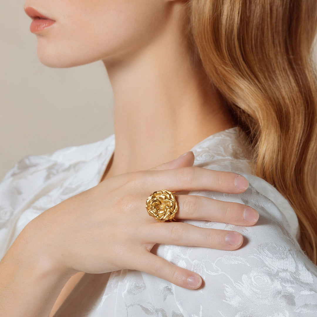 Woman wearing a gold floral statement ring on her finger while dressed in a white floral blouse