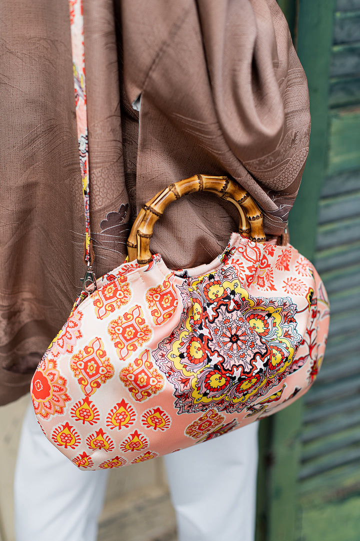 Person holding stylish pink handbag with vibrant floral pattern and bamboo handle