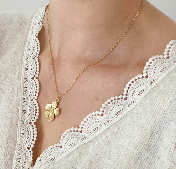 Gold floral pendant necklace on person wearing white lace-trimmed blouse