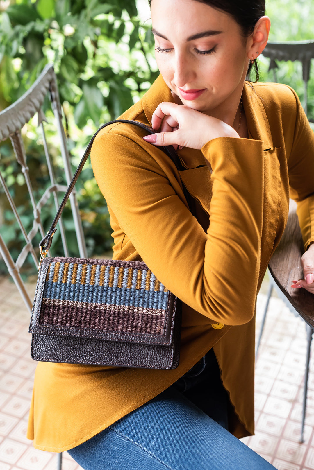 Woman wearing a mustard blazer and holding a stylish woven handbag at a cafe