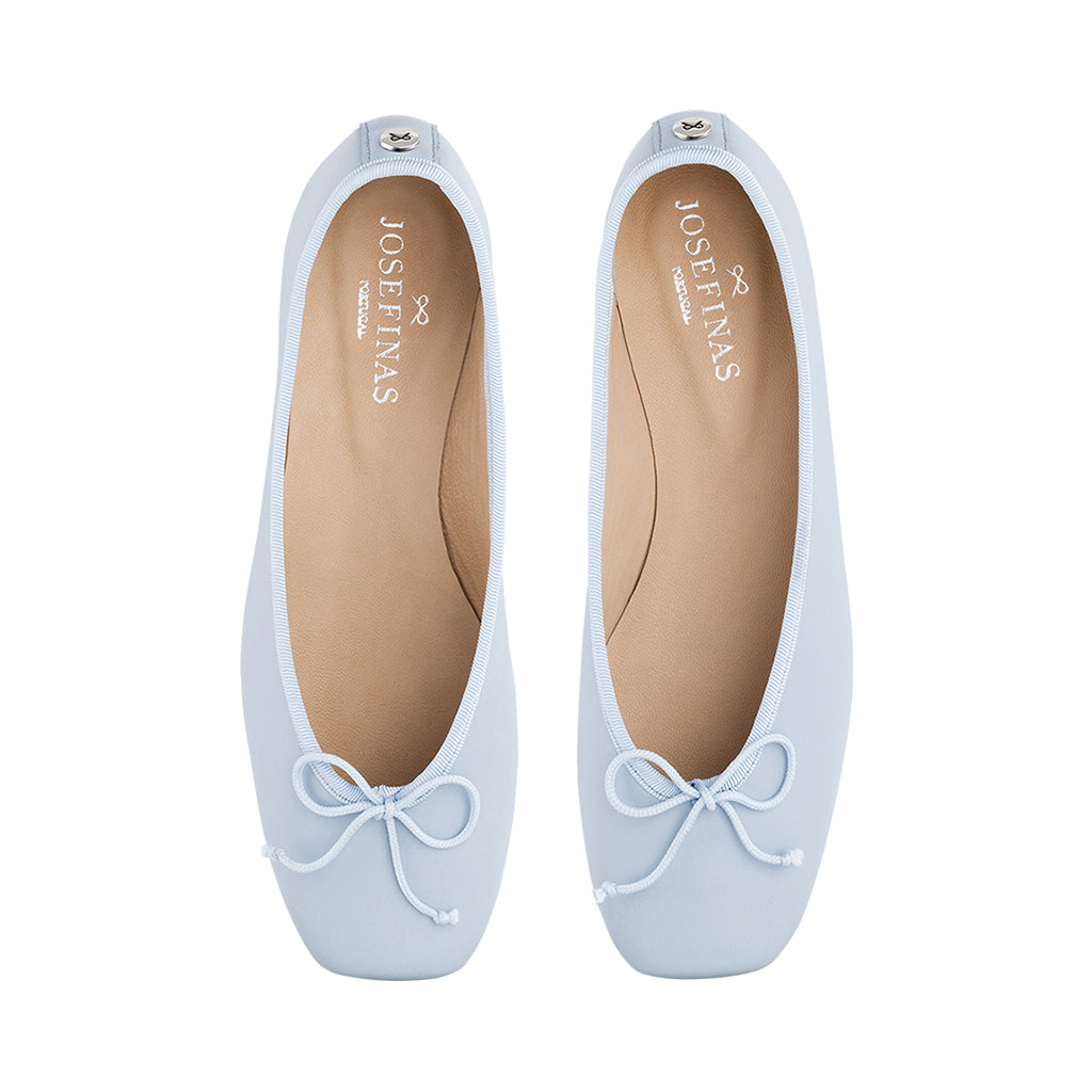 Light blue ballet flats with bows against a white background