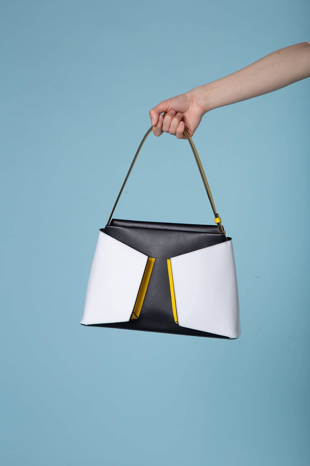 Hand holding a stylish black, white, and yellow handbag against a blue background