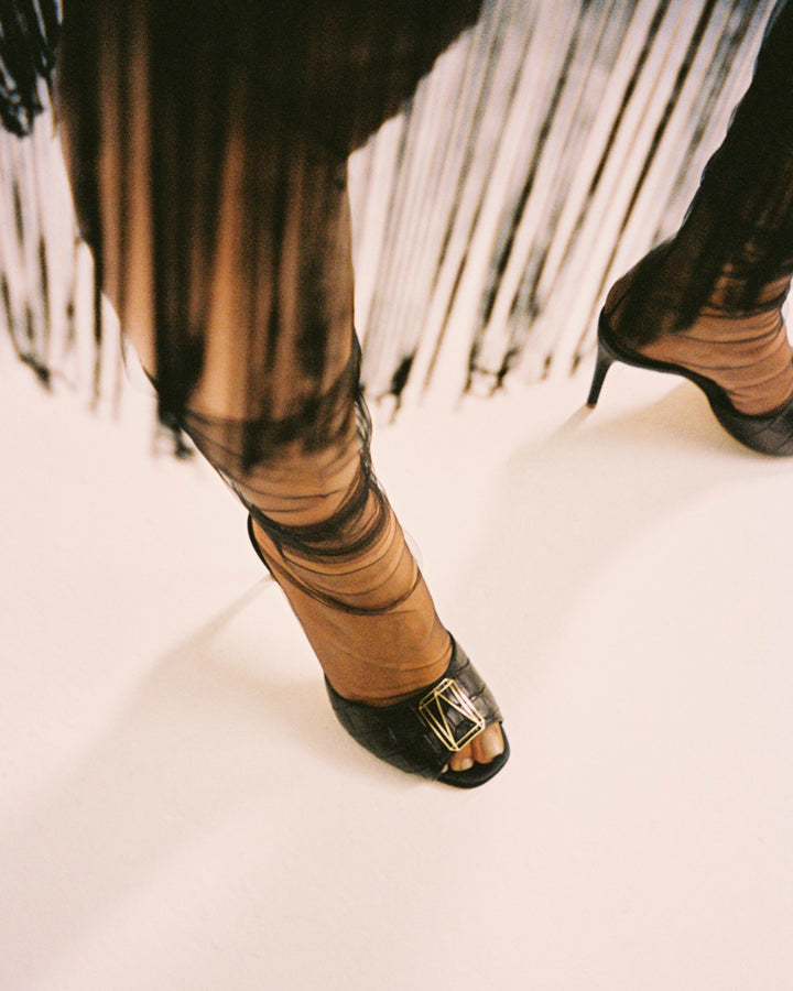 A close-up of stylish high heels with sheer black fabric and gold buckle detailing