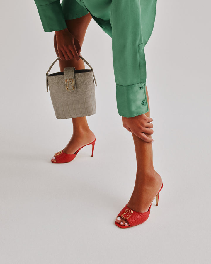 Woman in green dress holding a beige handbag and wearing red high heel shoes