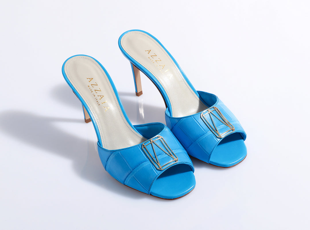 Blue high-heeled sandals with gold buckle detail on white background