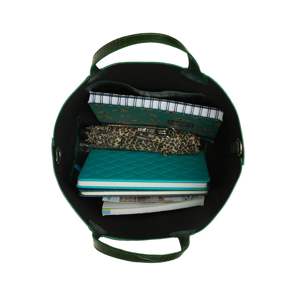 Top view of an open green handbag filled with notebooks, a pen, a leopard print pouch, and other items