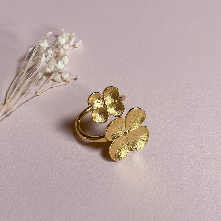 Gold floral ring against a pink background with white dried flowers