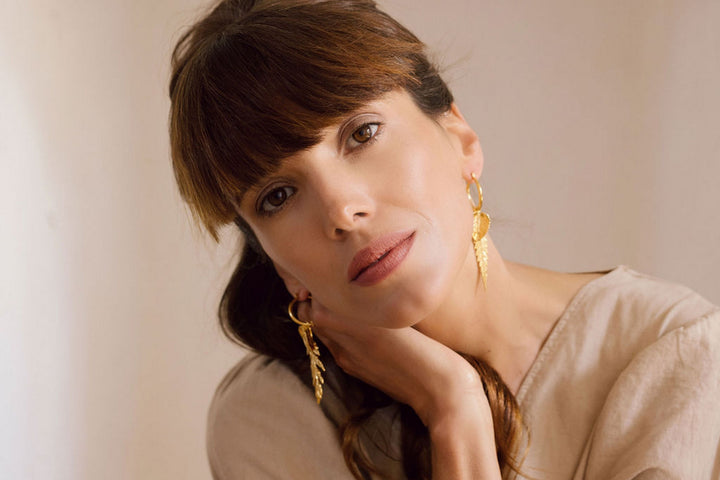 Woman wearing gold earrings and neutral top with hand near face