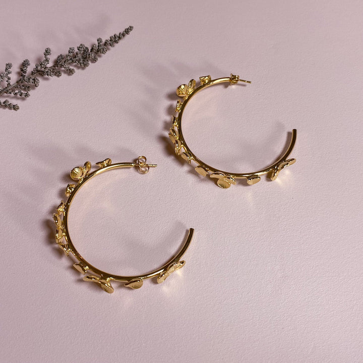 Gold floral hoop earrings on pink background