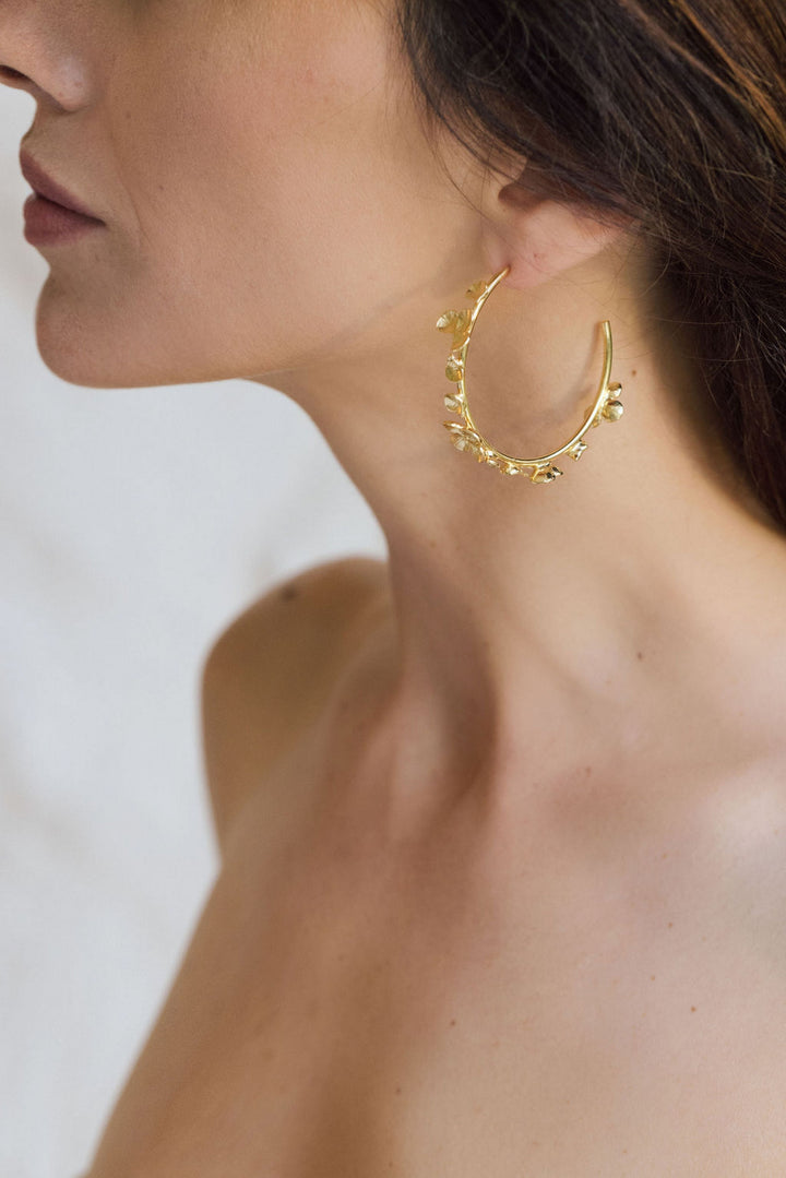 Close-up of woman wearing large gold hoop earring with floral design