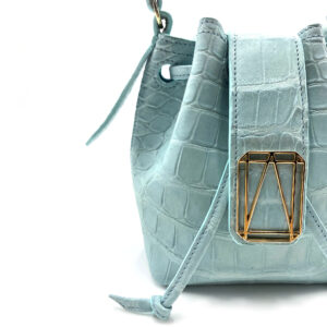 Light blue crocodile pattern handbag with gold hardware and drawstring closure against white background